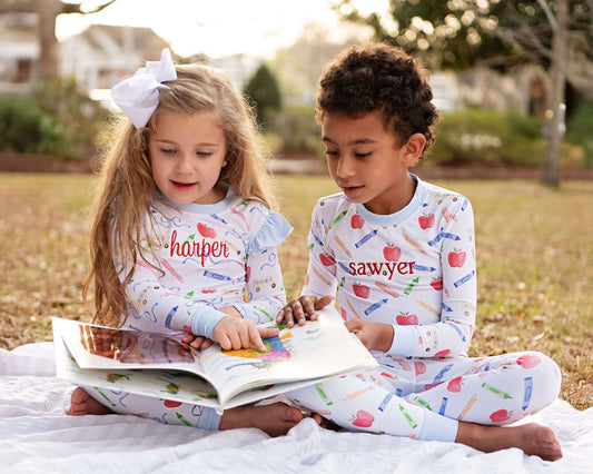 Two kids sitting on a blanket looking at a book