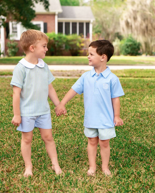 Two young boys holding hands on a grassy lawn with a house in the background