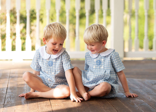 Two young boys in matching outfits sitting on a wooden floor.