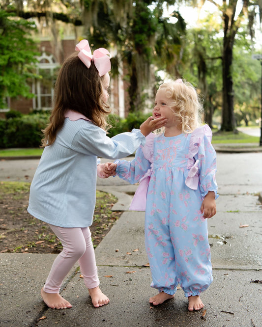 Two young children wearing matching light blue and pink pajama sets, standing on a wet sidewalk outdoors with trees in the background.