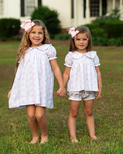 Two young girls holding hands in matching dresses with floral patterns outdoors.