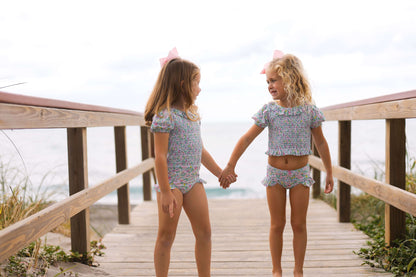 Two young girls holding hands on a wooden boardwalk by the beach.