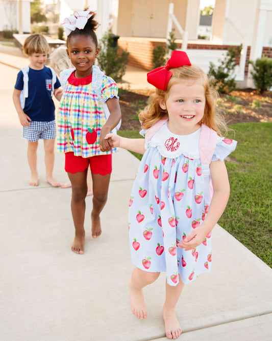 Two young girls in colorful outfits walking outdoors with a boy in the background.