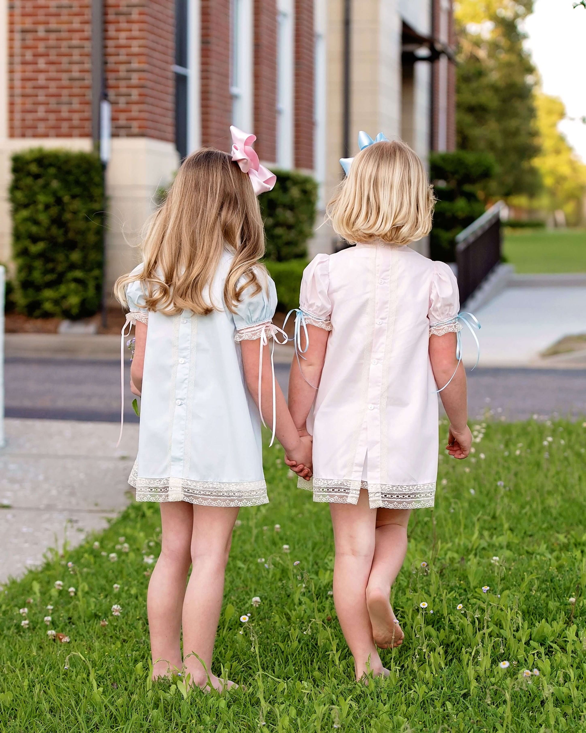 Two young girls in matching dresses standing on grass, holding hands.