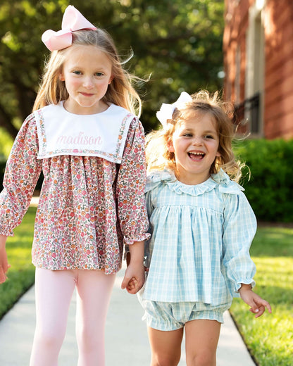 Two young girls in floral and checkered outfits walking outdoors.