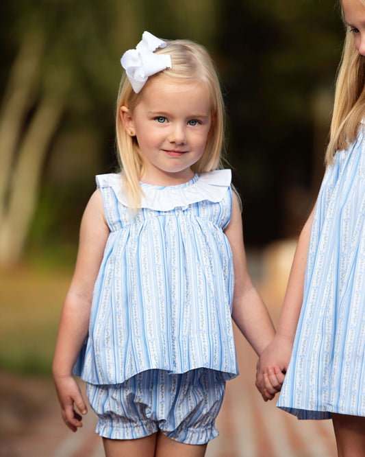 Two young girls in matching blue and white striped outfits standing outdoors.