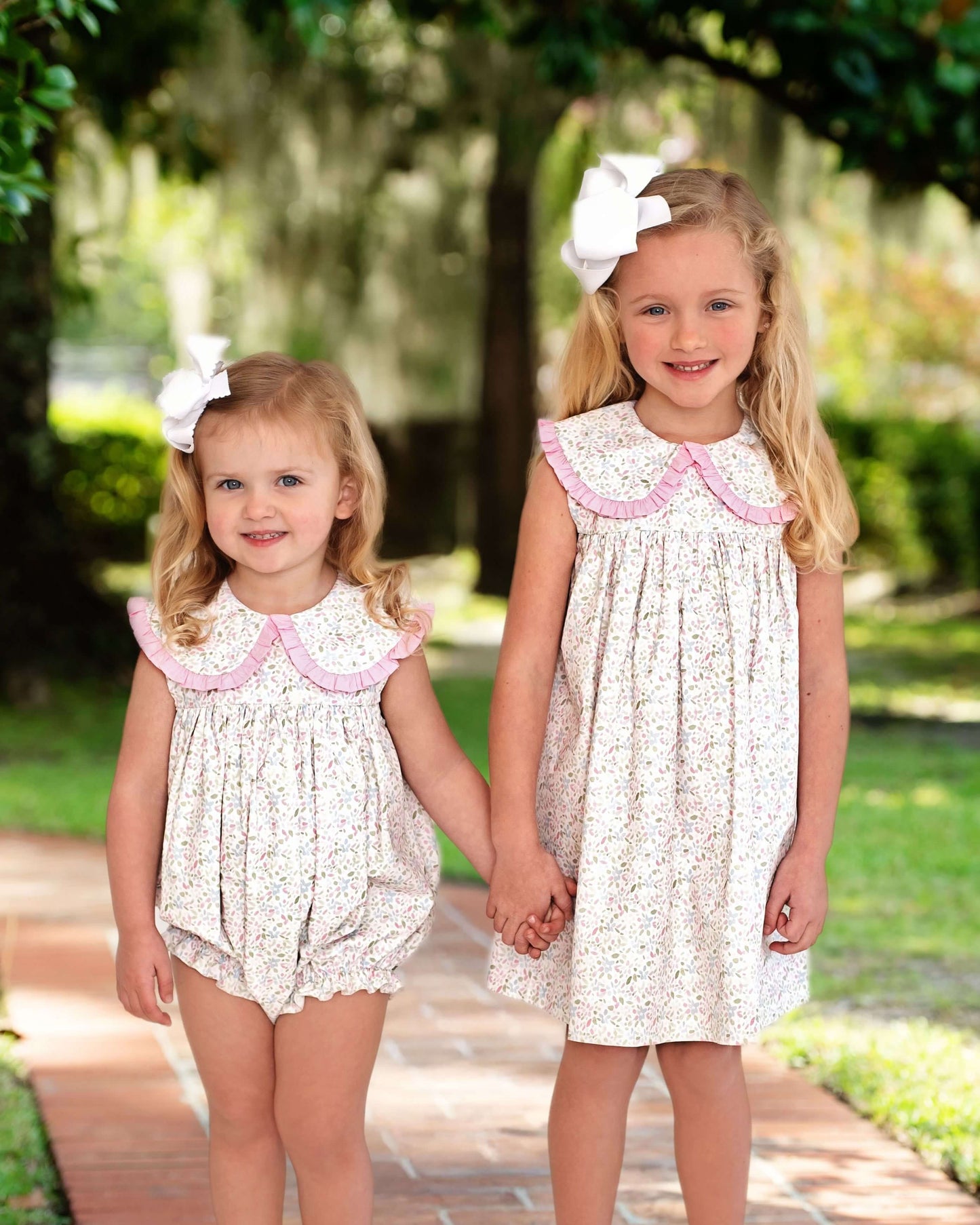 Two young girls in matching dresses holding hands outdoors.