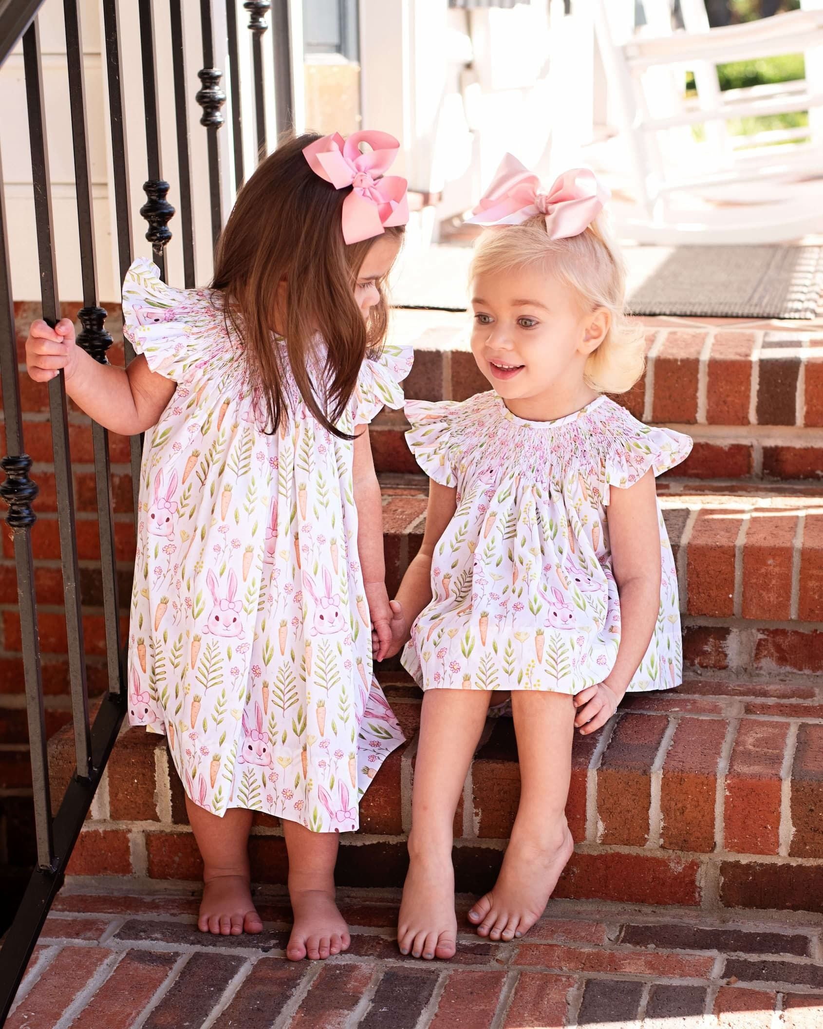 Two young girls in matching dresses sitting on a brick step.