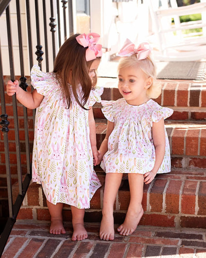 Two young girls in matching dresses sitting on a brick step.
