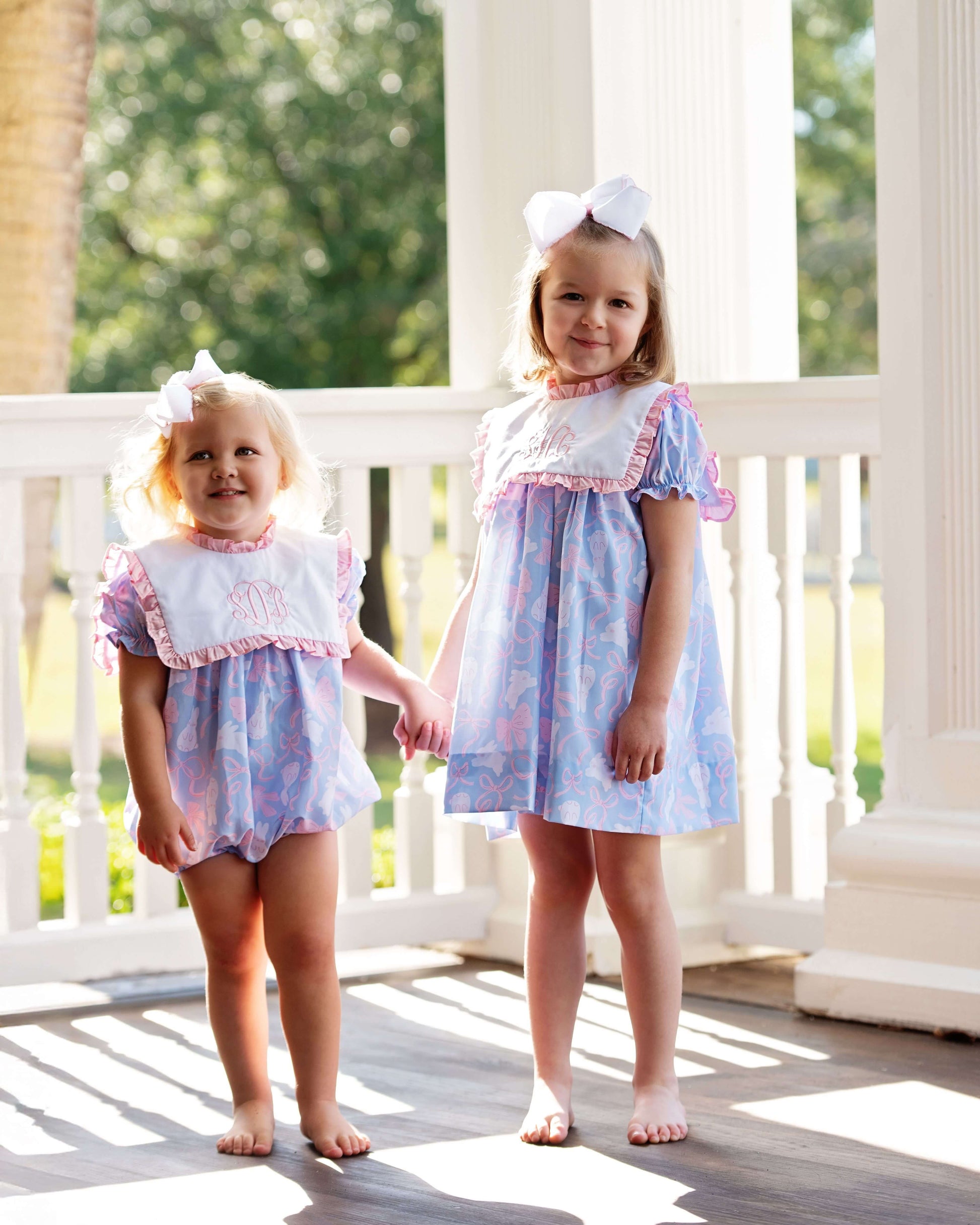 Two young girls in matching dresses standing on a porch.