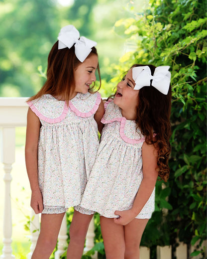 Two young girls in matching dresses with large white bows outdoors.