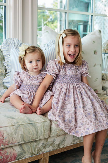 Two young girls in matching floral dresses sitting on a couch.