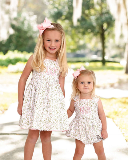 Two young girls in matching floral dresses with pink bows standing outdoors.