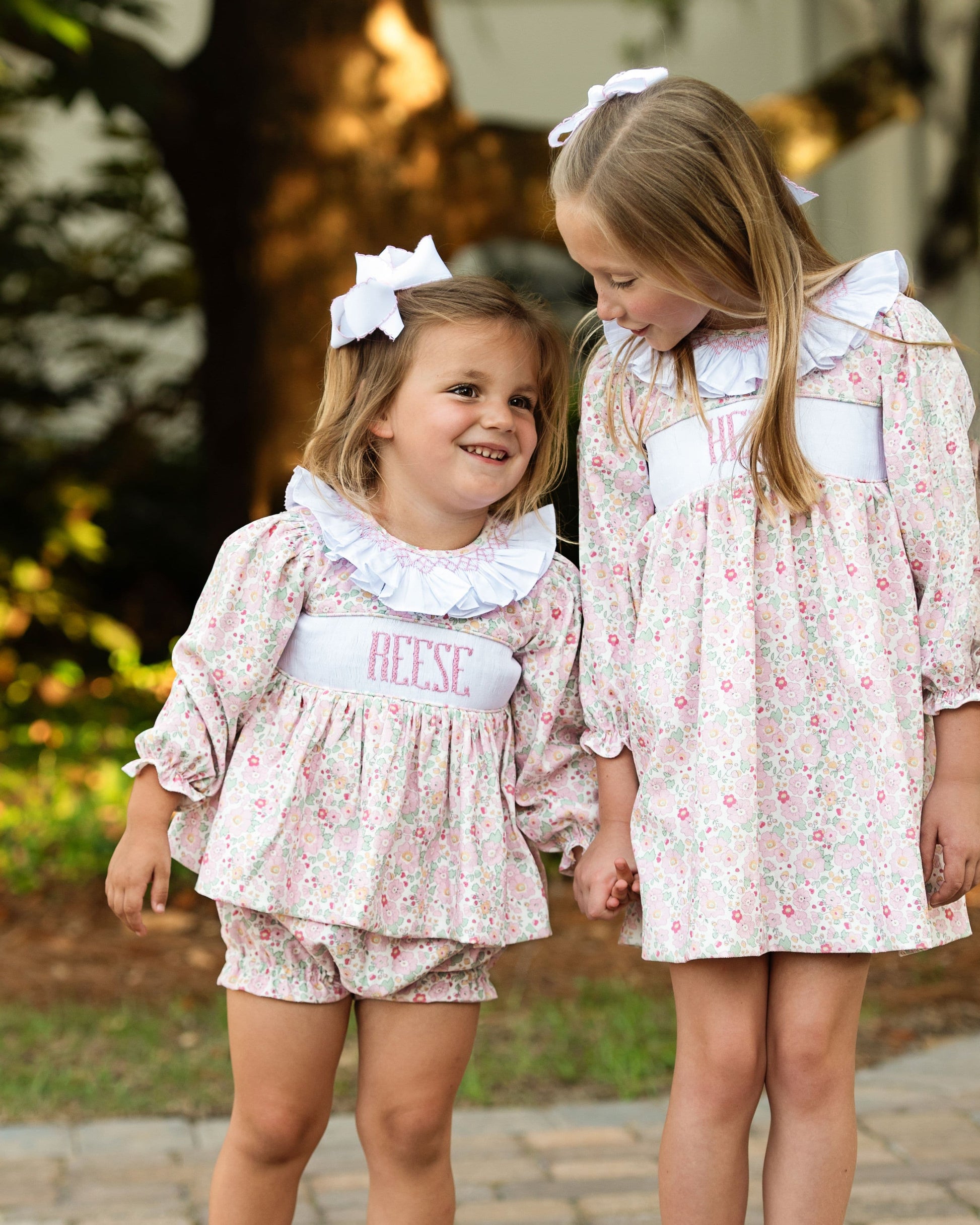 Two young girls in matching floral outfits standing outdoors.