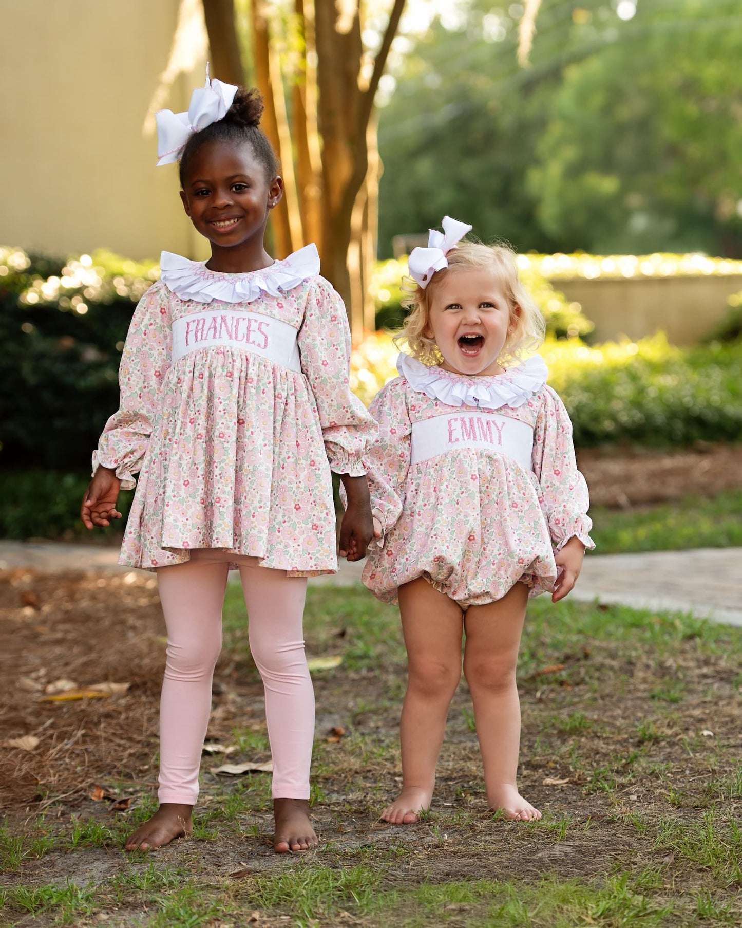 Two young girls in matching floral outfits with name labels outdoors.