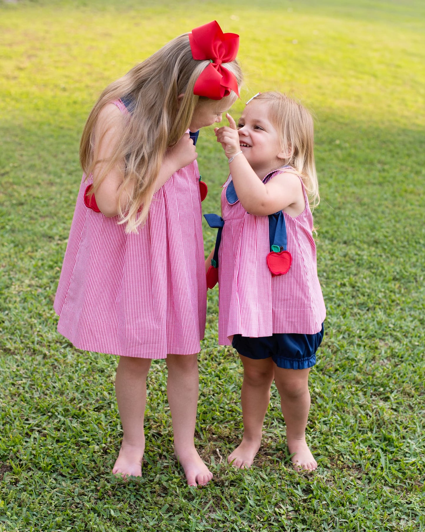 Two young girls in matching outfits standing on the grass.