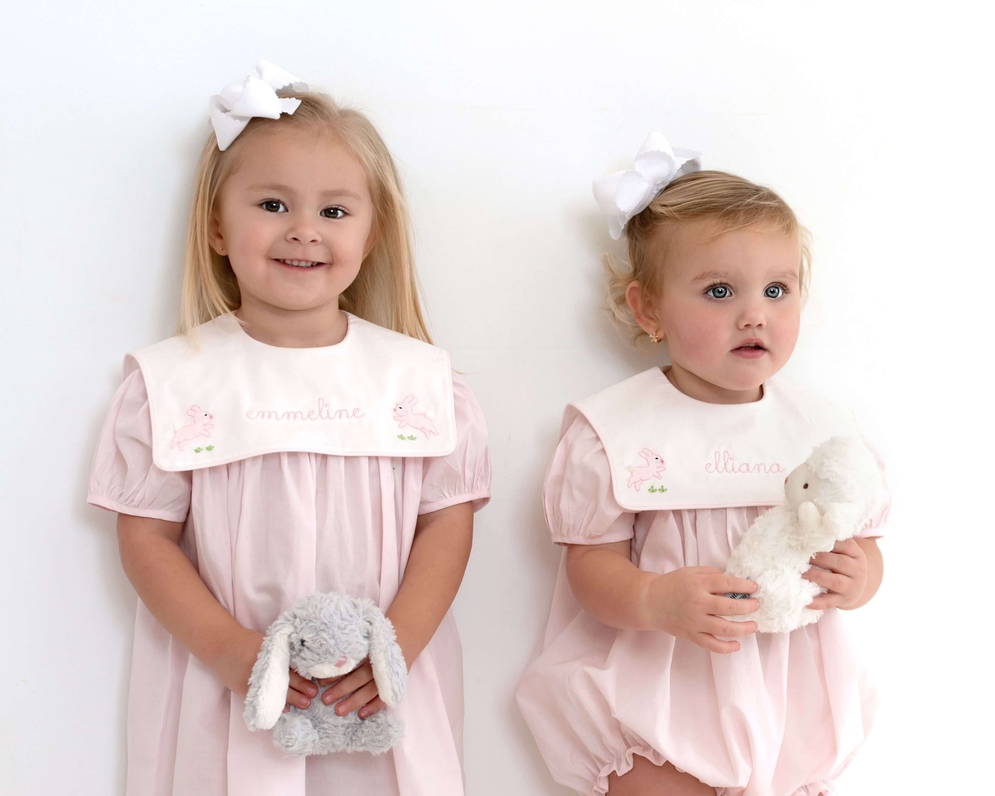 Two young girls in matching pink dresses holding stuffed animals against a white background