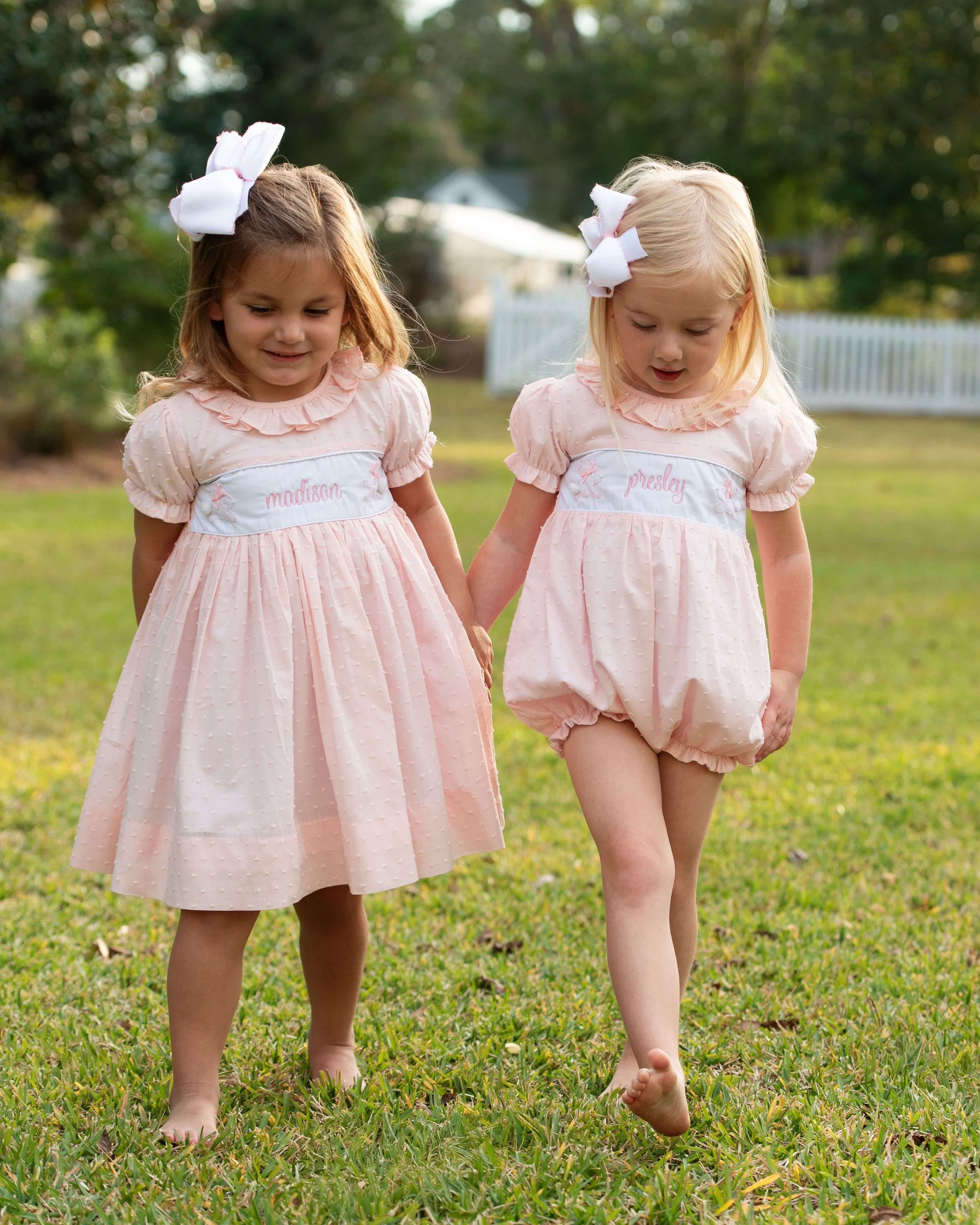 Two young girls in matching pink dresses walking on grass.