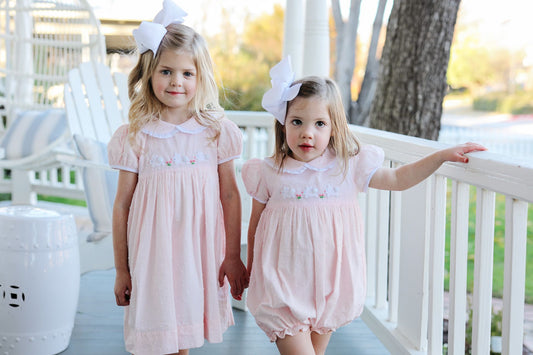 Two young girls in matching pink outfits standing on a porch.