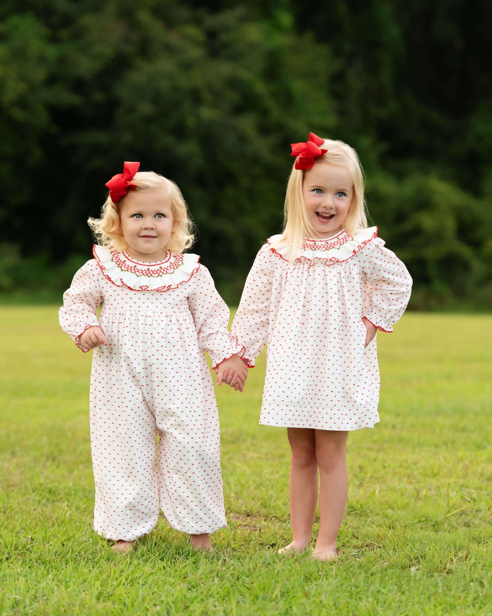 Two young girls in matching polka dot outfits with red bows standing in a grassy field.