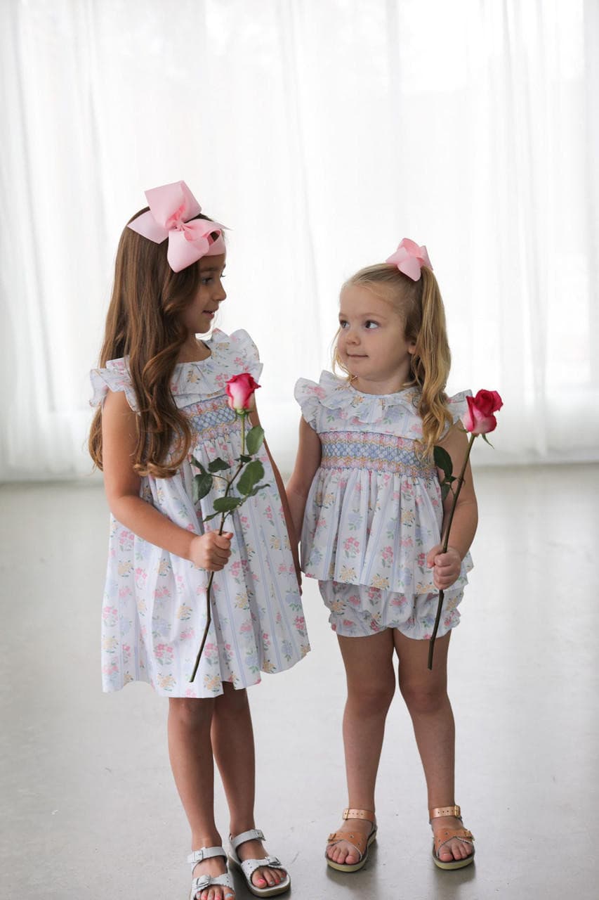 Two young girls in matching smocked outfits holding flowers against a white background