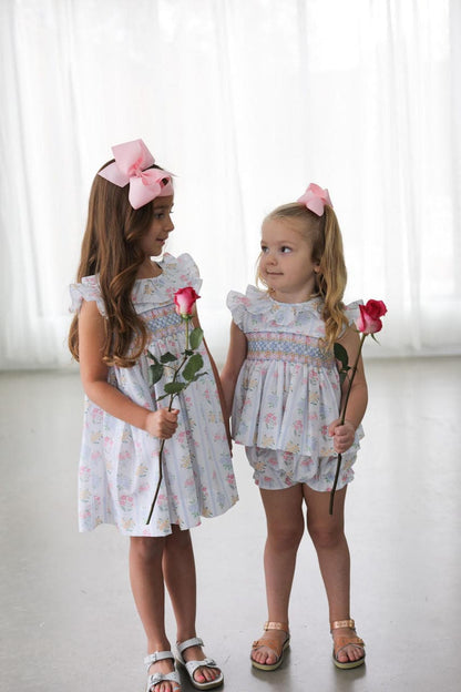 Two young girls in matching smocked outfits holding flowers against a white background