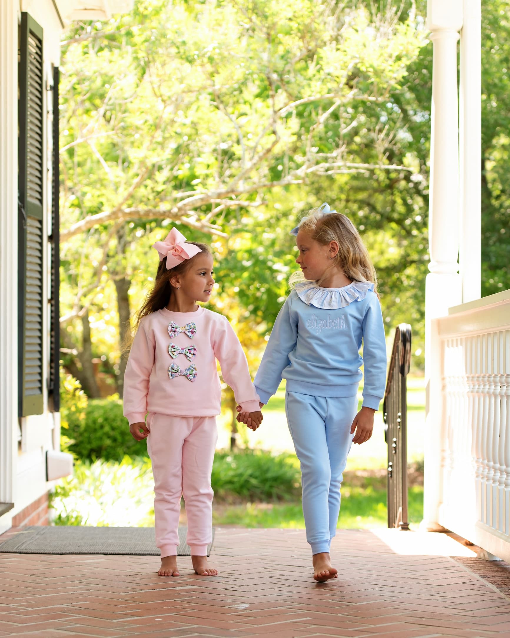 Two young girls in matching outfits walking on a porch.