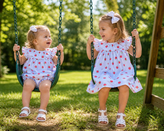 Two young girls wearing apple print outfits on swings. 