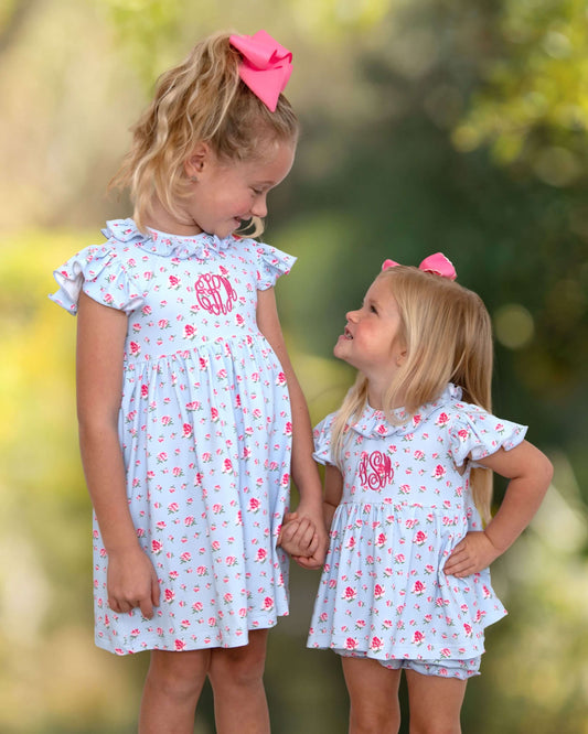Two young girls wearing matching dresses with a floral pattern outdoors.