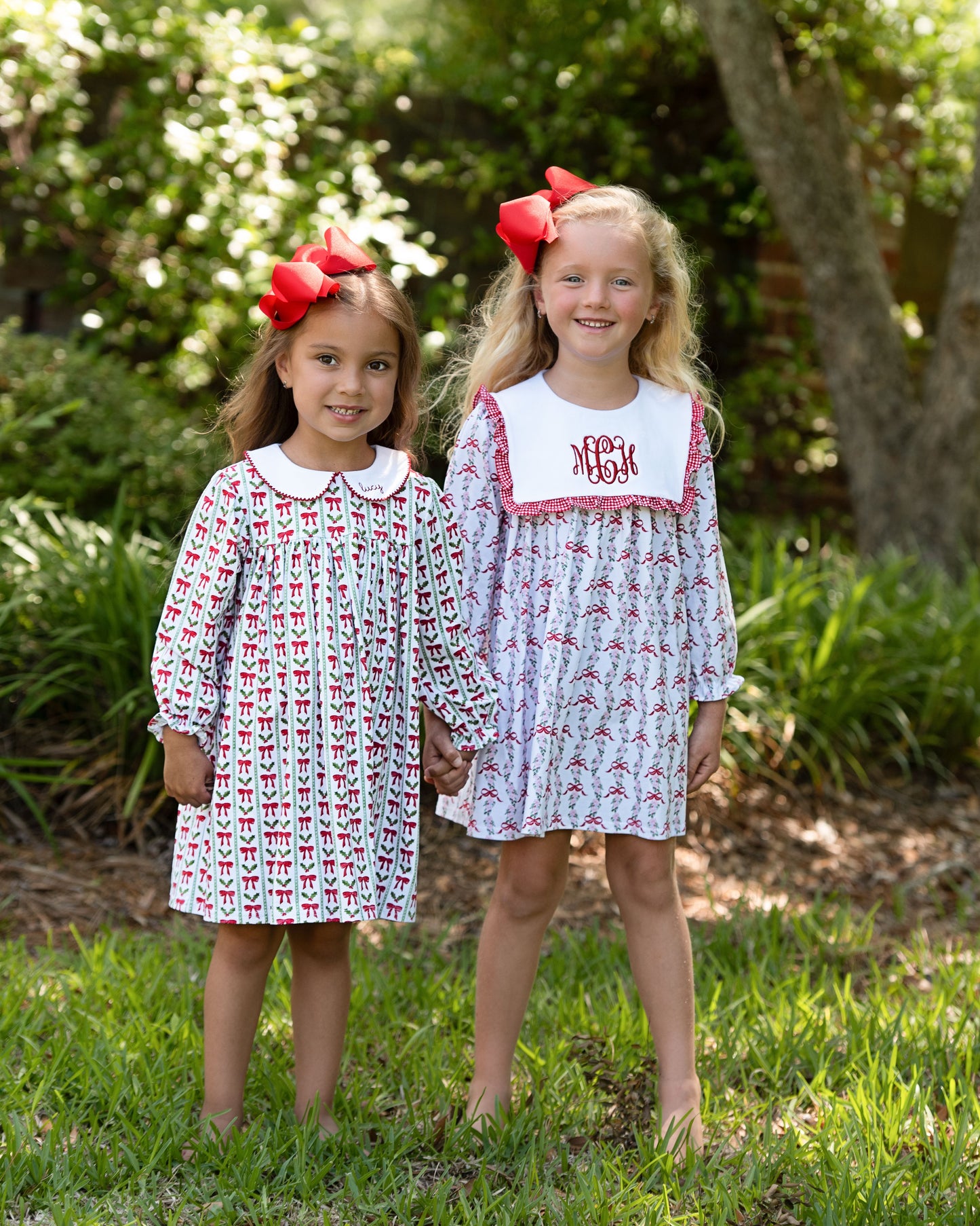 Two young girls wearing matching dresses with red bows outdoors.