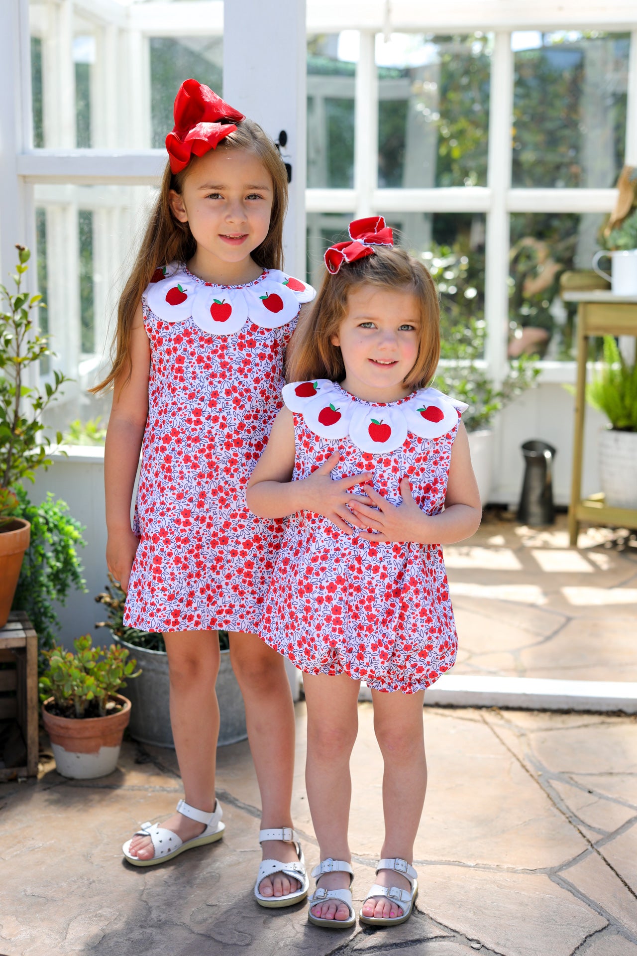 Two young girls wearing matching floral outfits with apples on it. 