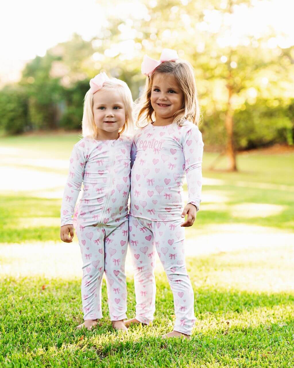 Two young girls wearing matching pajamas standing in a grassy outdoor area.