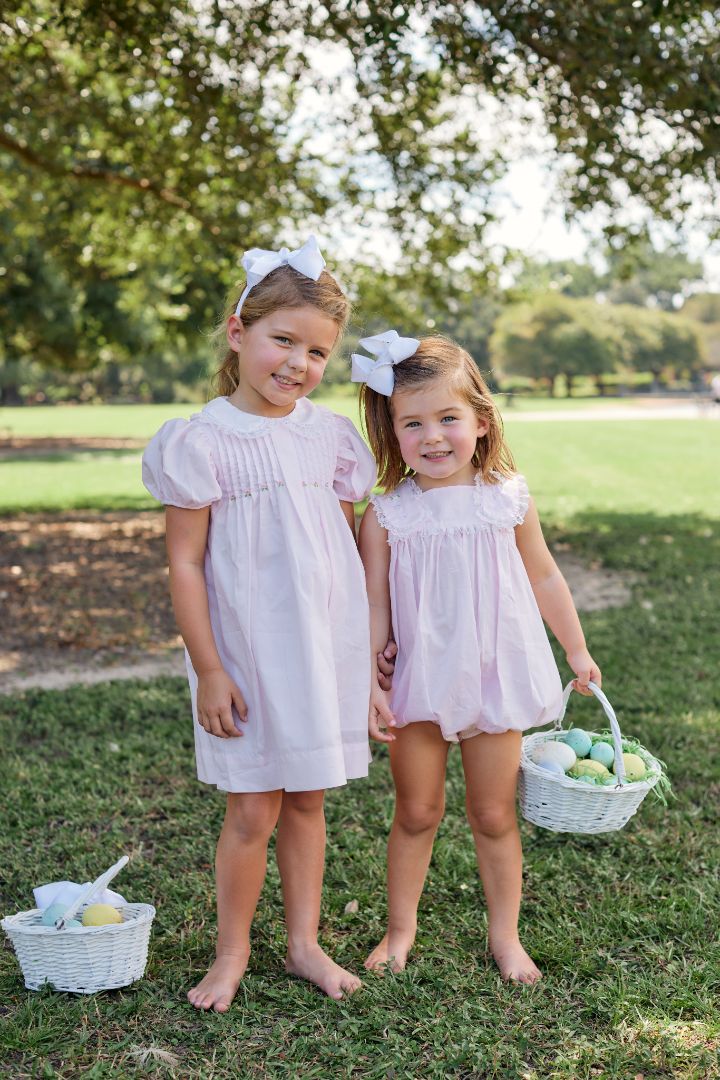 Two young girls wearing matching pink outfits, standing outside with Easter baskets
