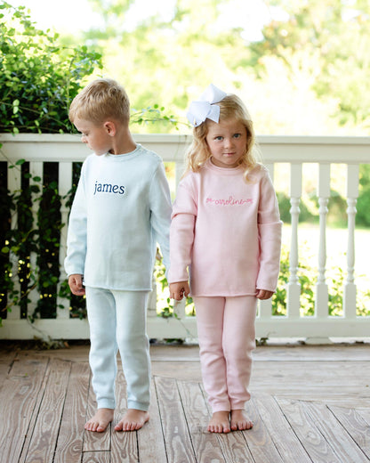 Two young kids standing on a porch in matching sweater outfits.