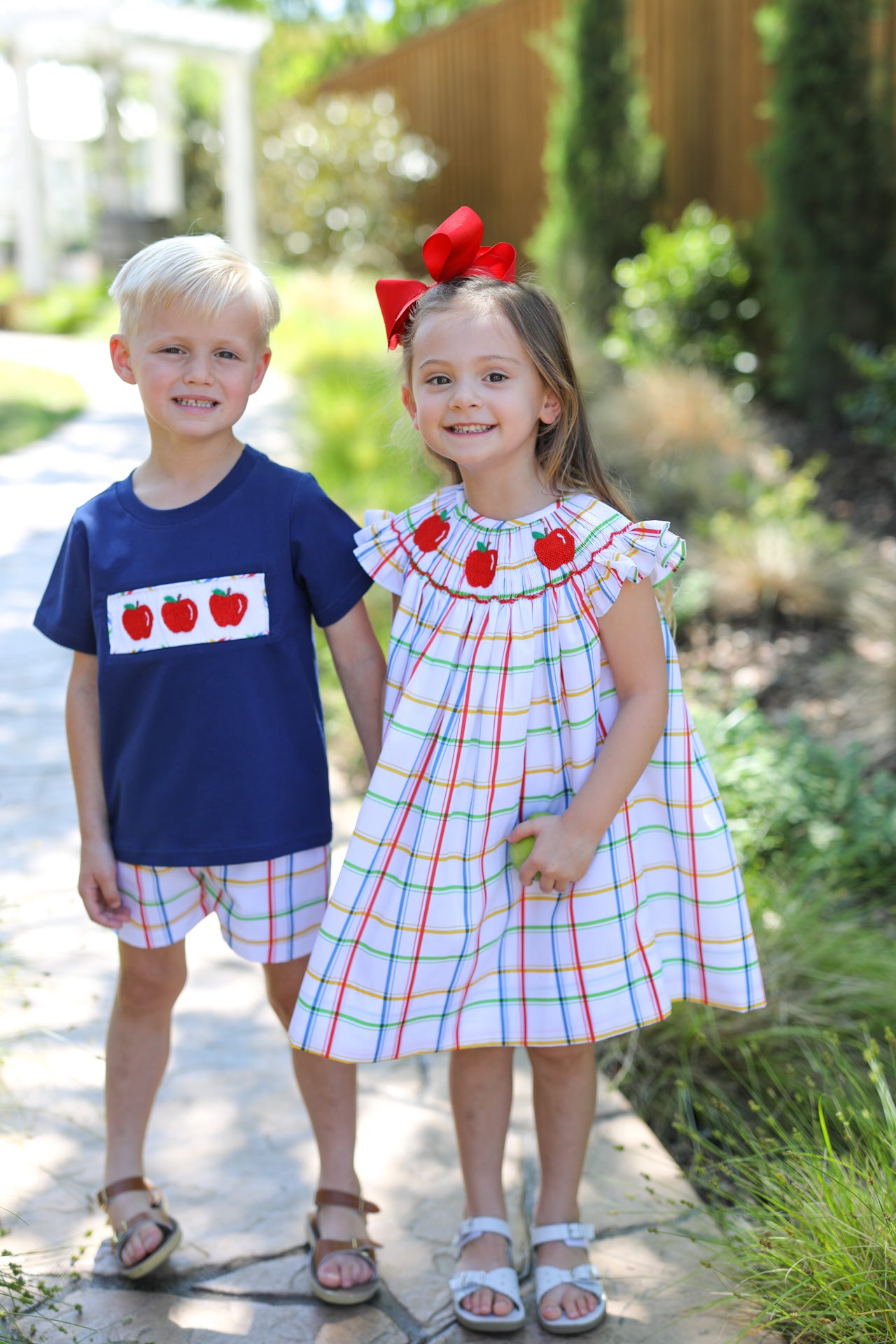 Two young kids wearing matching outfits with smocked apples on it.