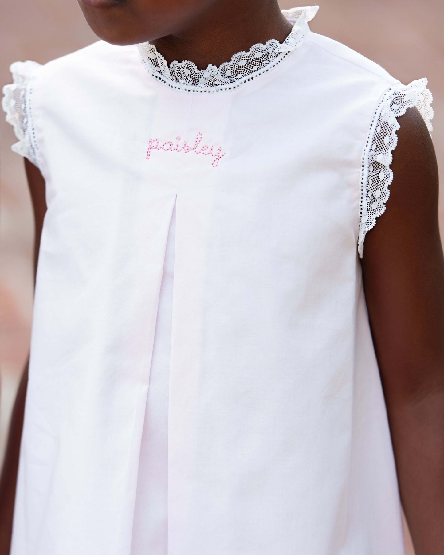 White dress with lace details and embroidered name on a blurred background