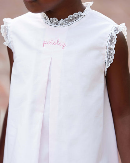 White dress with lace details and embroidered name on a blurred background