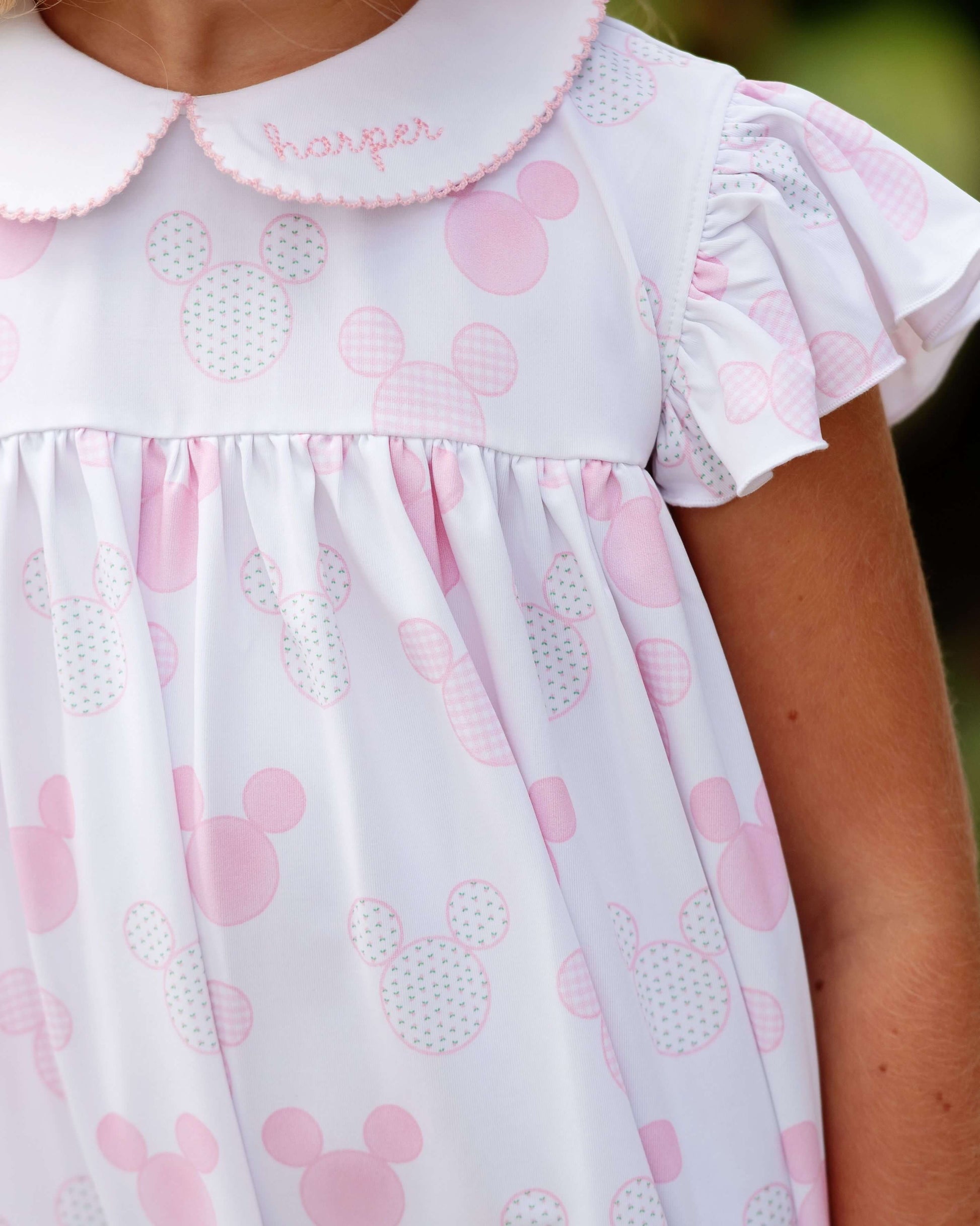 White dress with pink patterns and 'Harper' embroidered on the collar, worn by a person.