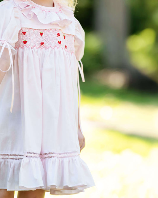White dress with red heart patterns worn by a person, blurred green background