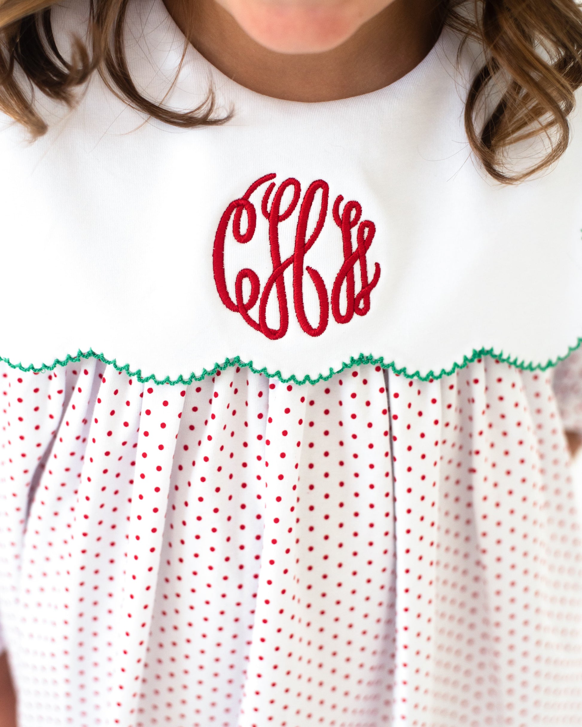White dress with red polka dots and green trim, featuring a red monogram on a white background.