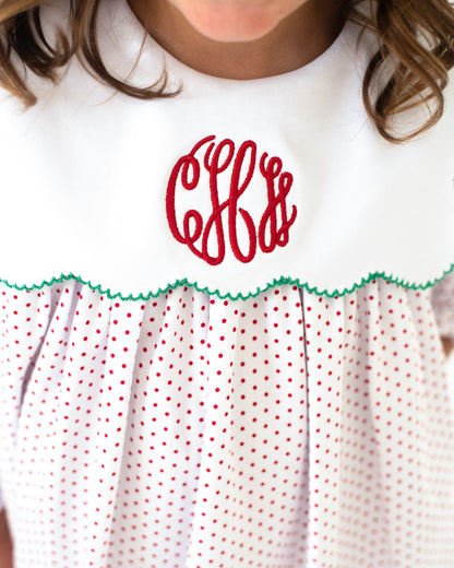 White dress with red polka dots and green trim, featuring a red monogram on a white background.