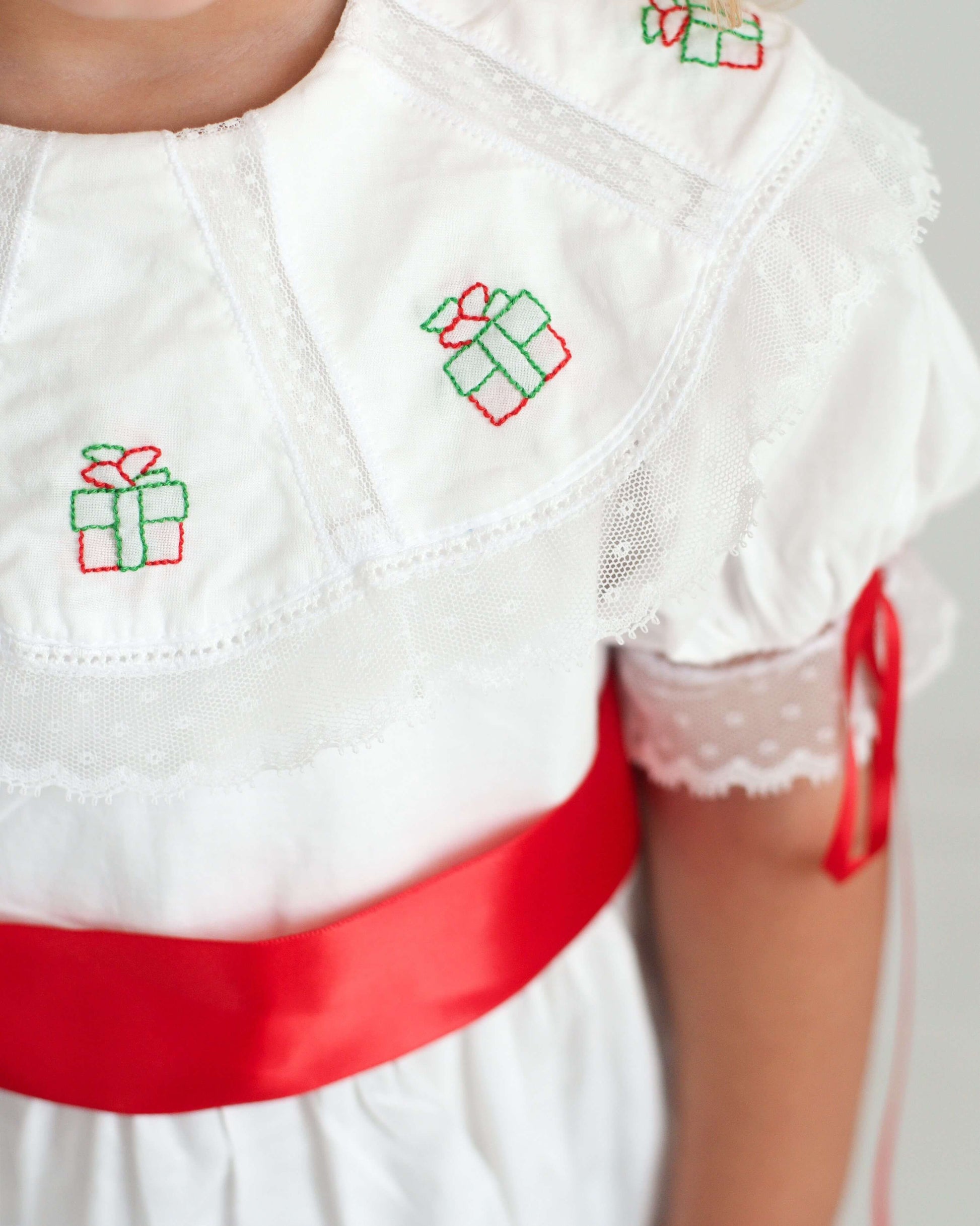 White dress with red ribbon and embroidered green gift boxes on a neutral background