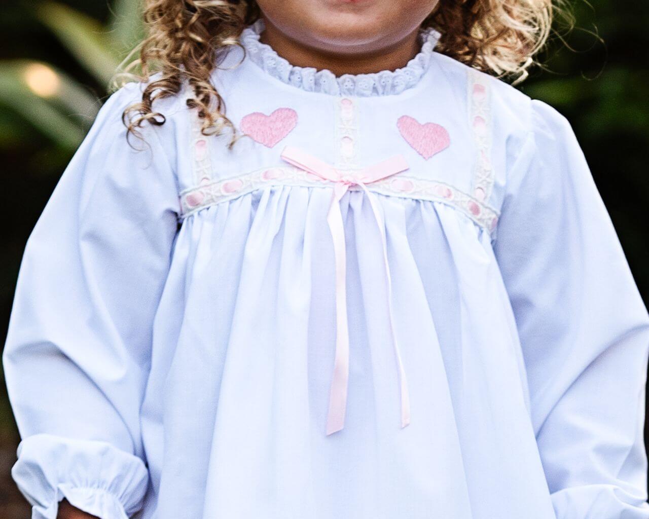 White nightgown with pink heart details worn by a child, blurred background
