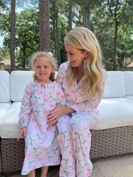 Woman and child in matching pink floral pajamas sitting on a white outdoor sofa with trees in the background.