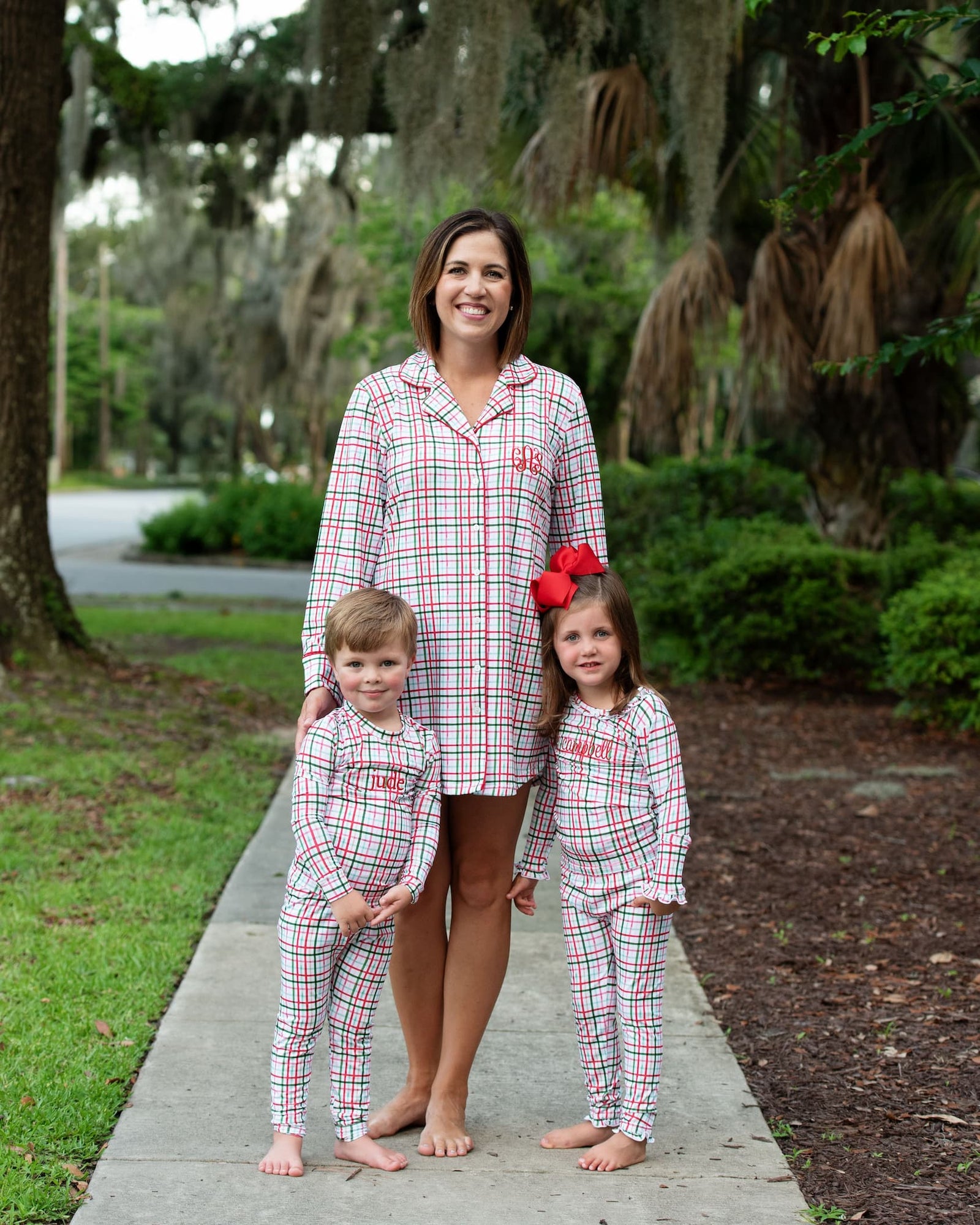 Mom and two children in matching red and green plaid windowpane pajamas outdoors