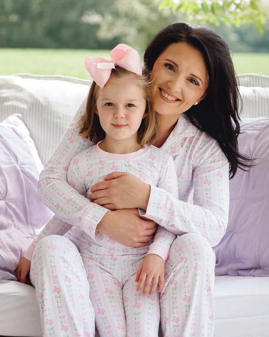 Woman and young girl wearing matching pajamas sitting on a couch outdoors.