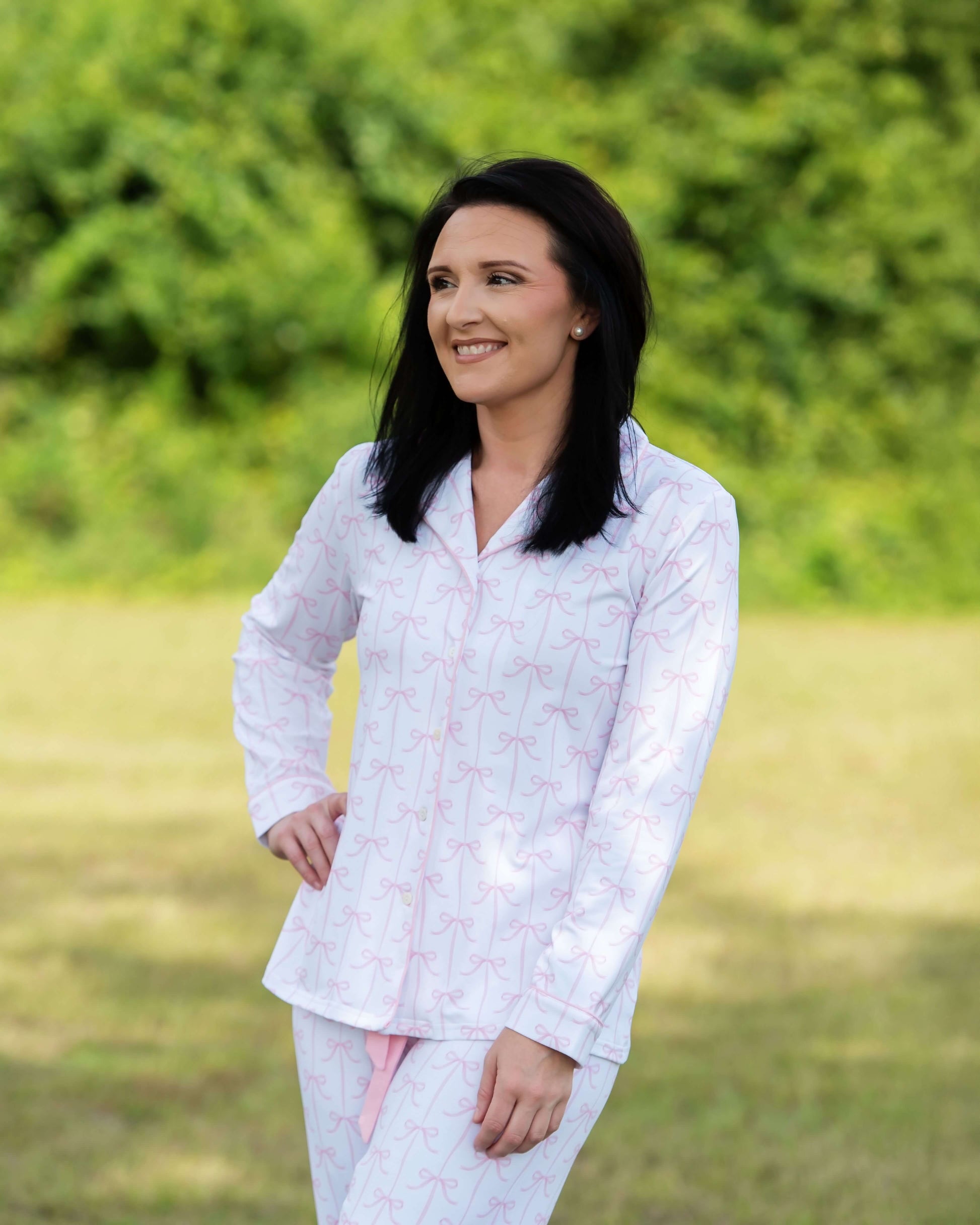 Woman wearing a white outfit with pink patterns standing in a grassy field.