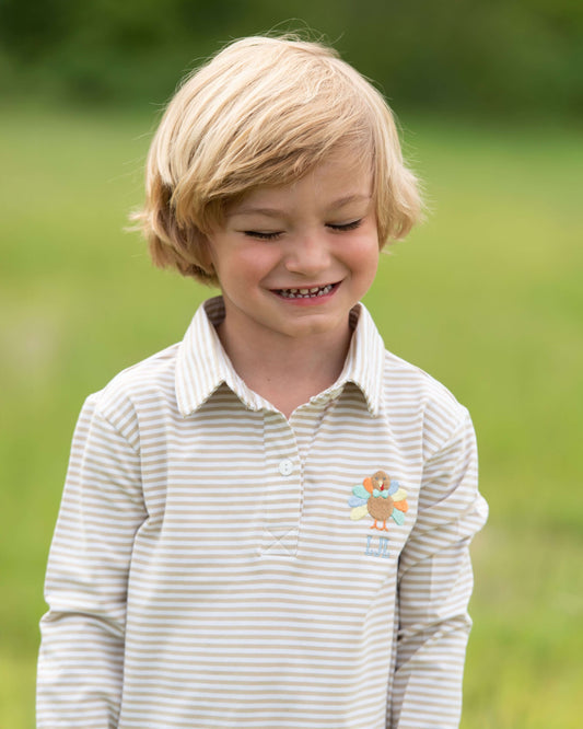 Young blonde boy wearing a striped shirt with a small turkey, standing outdoors.