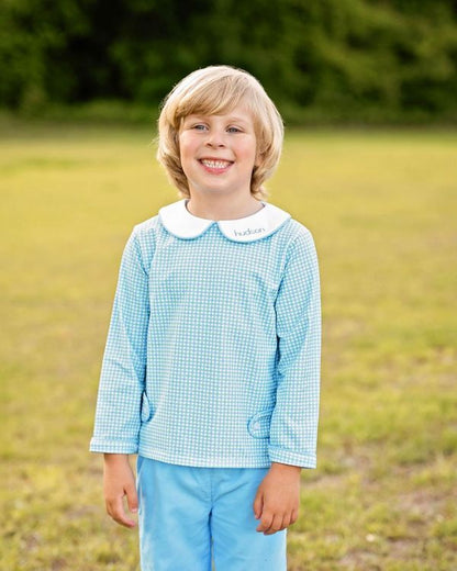 Young boy in a blue checkered shirt and light blue pants standing in a grassy field.