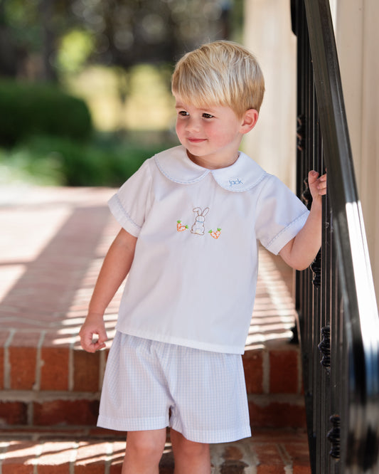Young boy in a light blue outfit standing outdoors near a building.